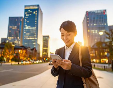 オフィス街でスマホを操作する女性社員の写真
