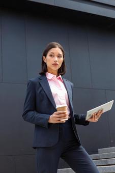 コーヒーとタブレットを持ってオフィスビルの外の階段を登る女性 ビジネスウーマン,ビジネス,女性の写真素材