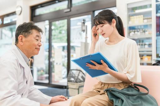薬局で問診票を書く女性と相談に乗る薬剤師 頭痛,薬局,問診票の写真素材