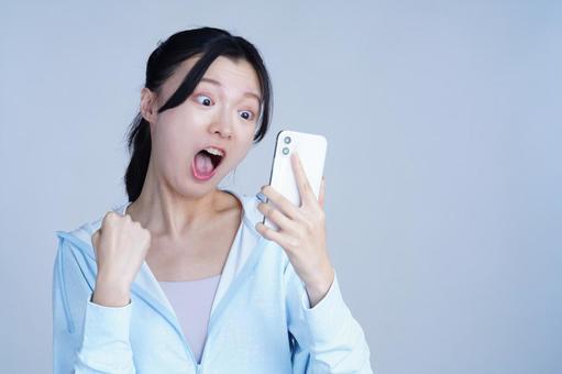 水色の服の女性がスマホを見て驚く 女性,スマートフォン,持つの写真素材