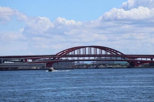 青い海と船と赤い橋と街並みと雲と青空の写真