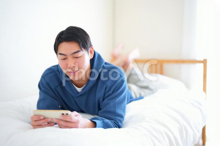 ベッドで腹ばいでスマートフォンを見ている男性 引っ越し,一人暮らし,男性の写真素材