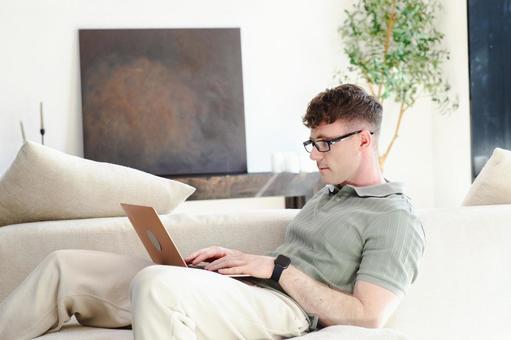 ソファに座って膝の上でノートパソコンを使うメガネの男性 男性,外国人,欧米人の写真素材