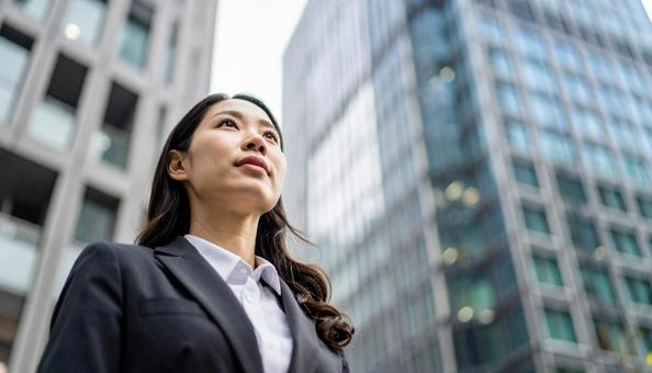 高層ビル背景にスーツの女性が空を見つめる 高層ビル背景にスーツの女性が空を見つめるの写真