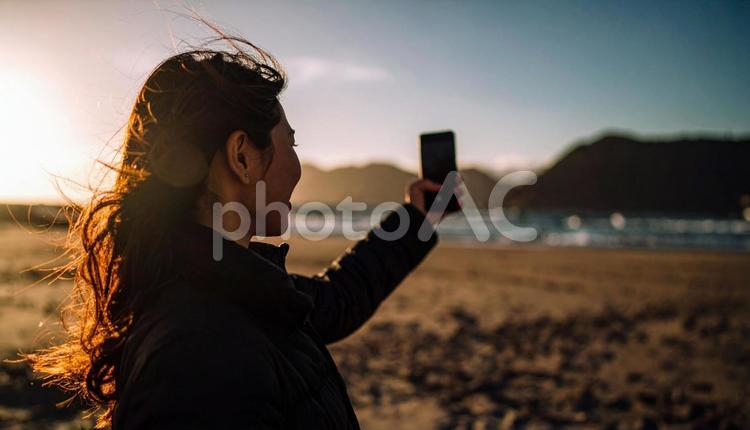 海辺でスマホで自撮りする日本人女性  海辺,スマホ,自撮りの写真素材