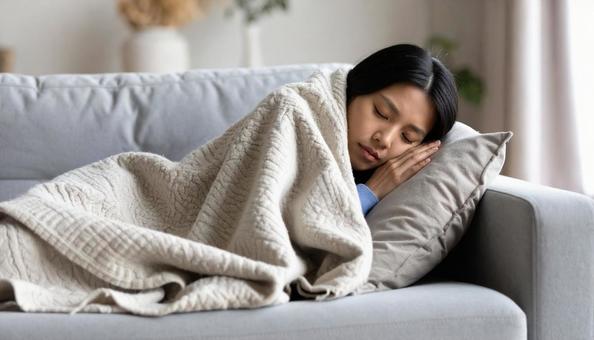 ソファで毛布にくるまって眠る若い女性 ソファで毛布にくるまって眠る若い女性の写真