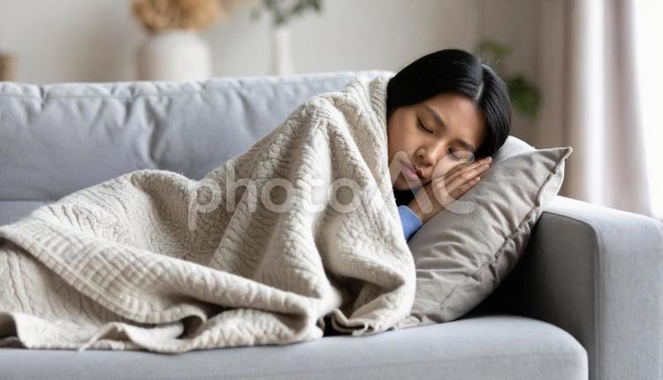 ソファで毛布にくるまって眠る若い女性 睡眠,休息,リラックスの写真素材