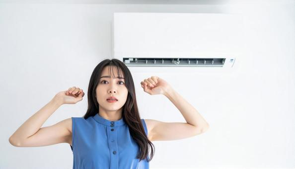 部屋のエアコンの下で寒がる女性 部屋のエアコンの下で寒がる女性の写真