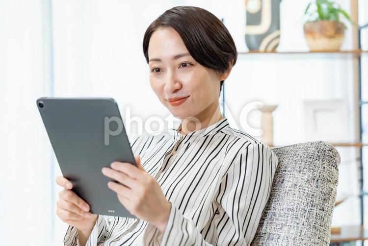 ソファに座りタブレットを見る女性 スマホ,ビジネス,メッセージの写真素材