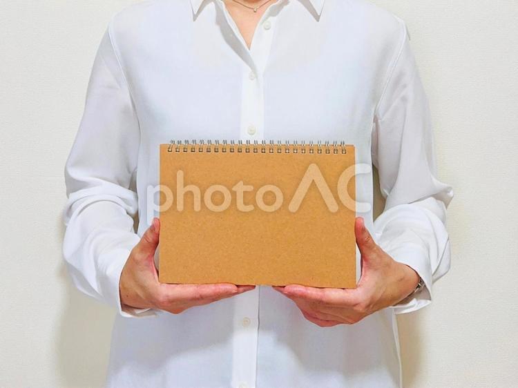 茶色いノートを掲げる女性社員 ノート,プレゼン,女性の写真素材