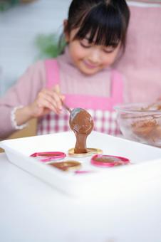 チョコレートを型に流し入れるエプロン姿の女の子 女の子,チョコレート,スプーンの写真素材