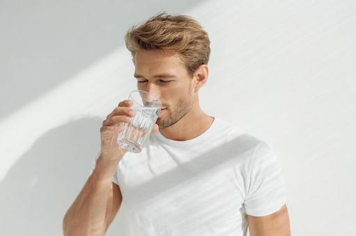 白いTシャツの男性がグラスの水を飲む 白いTシャツの男性がグラスの水を飲むの写真