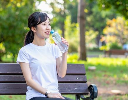 公園のベンチで水を飲む女性 公園のベンチで水を飲む女性の写真
