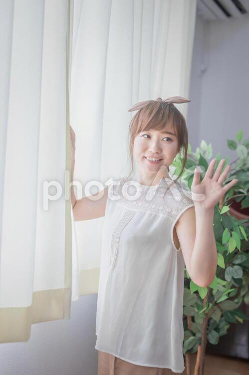 朝日が差し込む明るい窓辺で手を振る若い女性 おはよう,窓,挨拶の写真素材