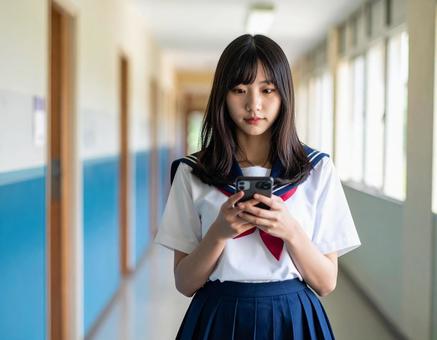 学校の廊下でスマホを見つめる女子学生 学校の廊下でスマホを見つめる女子学生の写真
