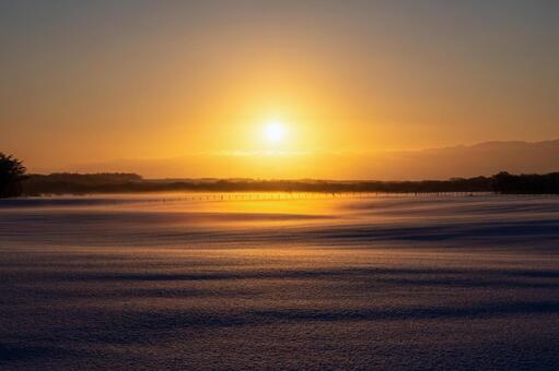 陽炎と雪煙が舞う、冬の牧場の日の出 朝焼け,日の出,牧場の写真素材