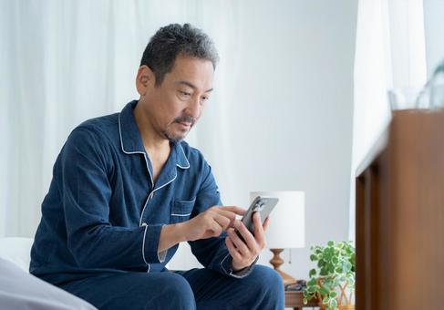 寝室でスマホを見るミドルの男性 寝室でスマホを見るミドルの男性 男性,スマホ,ミドルの写真素材