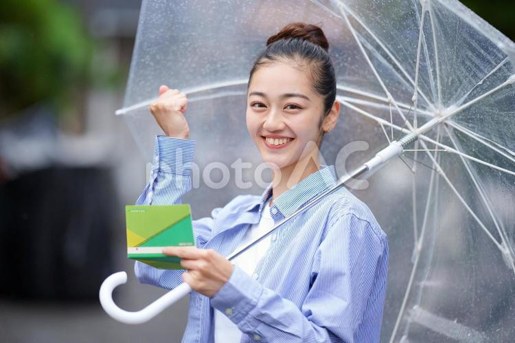 透明な傘を差して通帳を持ってガッツポーズの女性 女性,雨,日本人の写真素材