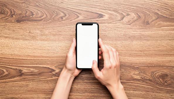 木製テーブルの上でスマホを操作する手元 木製テーブルの上でスマホを操作する手元の写真