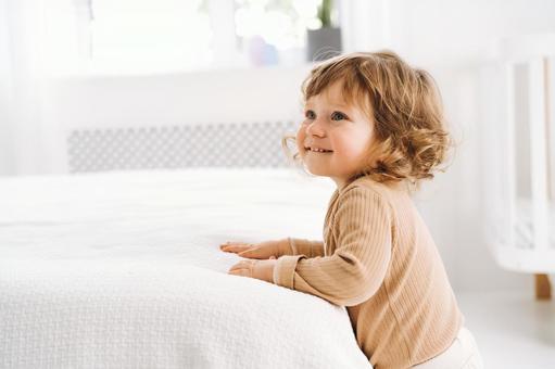 ベッドにつかまり立ち笑う子供 ベッドにつかまり立ち笑う子供 赤ちゃん,かわいい,ベッドの写真素材