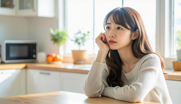 疲れた表情でキッチンに座る若い女性 疲れた表情でキッチンに座る若い女性の写真