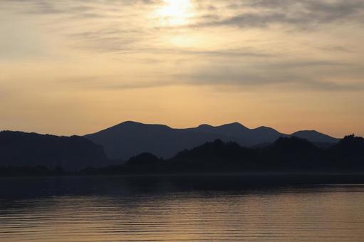 さざ波の湖面の湖と山と朝焼けの空と太陽 さざ波の湖面の湖と山と朝焼けの空と太陽の写真