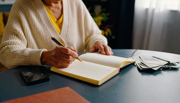家計簿をつけるシニア女性の手もとの写真