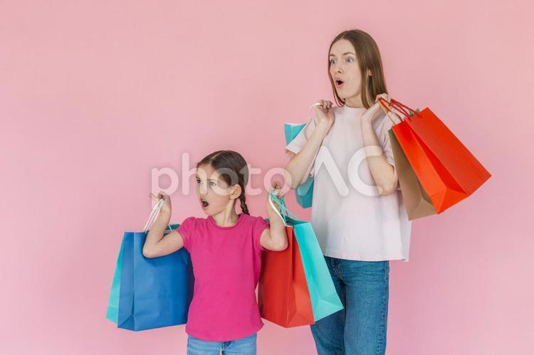 両手に紙袋を持って遠くを見て驚く親子２ 女性,女の子,親子の写真素材