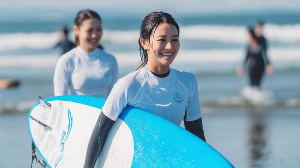 海辺の砂浜でサーフボードを抱え歩く女性 海辺の砂浜でサーフボードを抱え歩く女性の写真