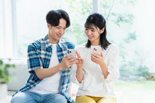 リビングでスマホを見るカップル リビングでスマホを見るカップル スマホ,笑顔,カップルの写真素材