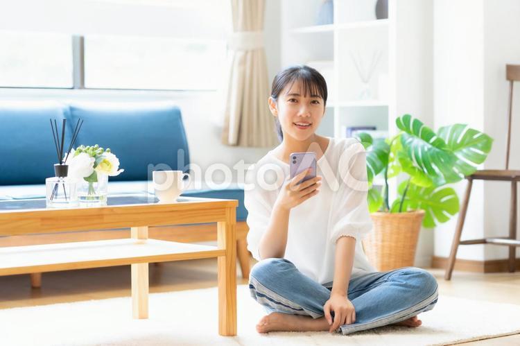 リビングでスマホを見る大学生の女性 女性,スマホ,大学生の写真素材