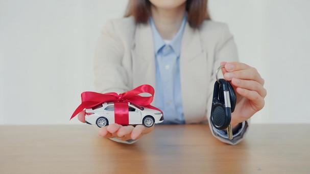 リボンを巻いた車の模型とストラップを渡そうとする手元 保険業,事務職,接客業の写真素材
