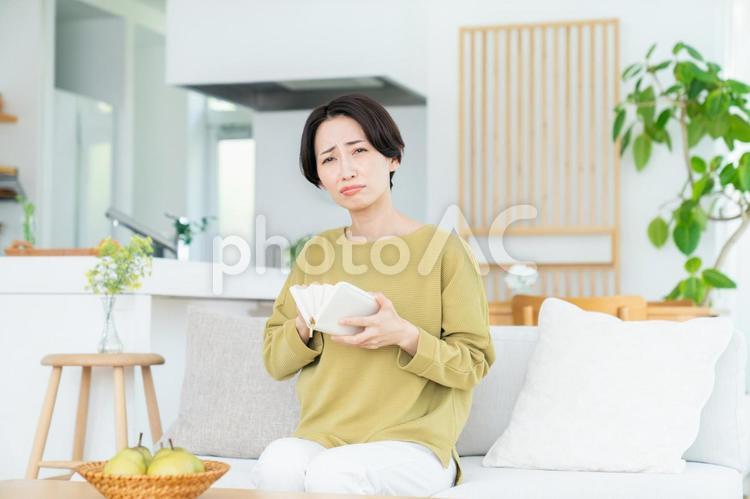 リビングで財布を持って悩むミドルの女性 財布,家計,お金の写真素材