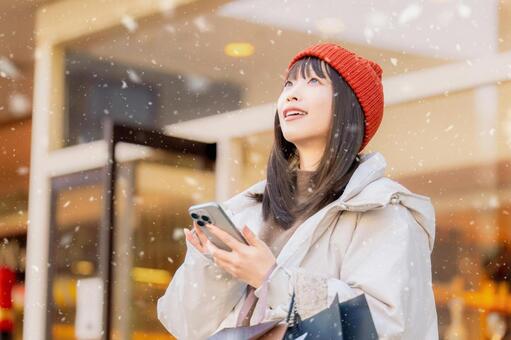 雪の降る冬の街角でスマホを使う女性 冬,雪,女性の写真素材