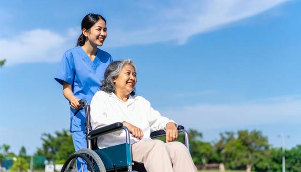 車椅子を押してシニア女性と笑う若い介護士 車椅子を押してシニア女性と笑う若い介護士の写真