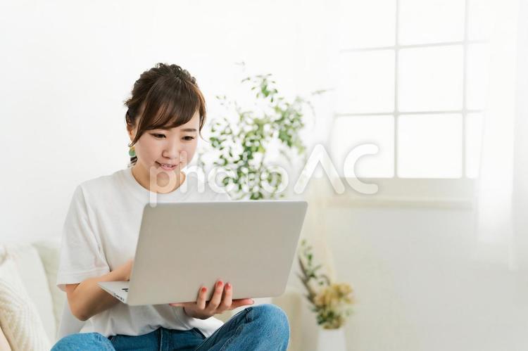 ソファでパソコンを見る日本人女性（笑顔） テレワーク,パソコン,女性の写真素材