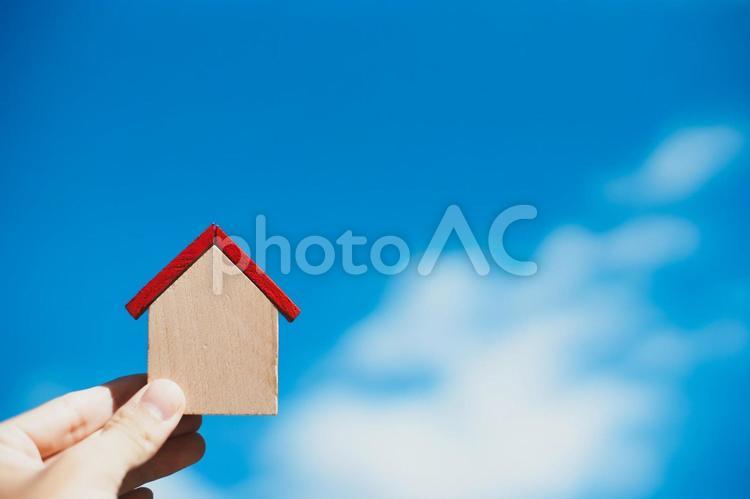 小さな木製の家を持つ人の手元と青空背景 家,住宅,青空の写真素材