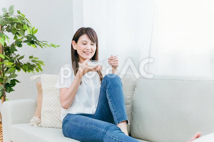 ソファでヨーグルトを食べる女性（笑顔） ヨーグルト,乳酸菌,菌活の写真素材