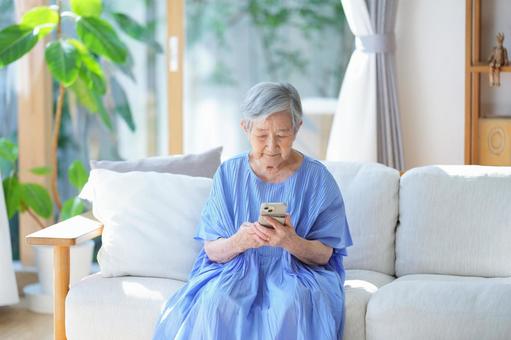 リビングでスマホを見ている高齢女性 女性,スマートフォン,持つの写真素材