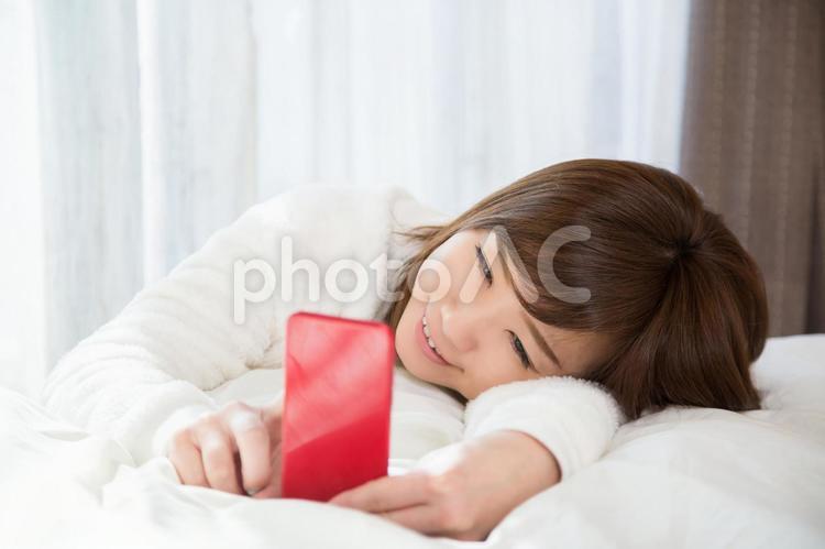 ベッドでスマホを見る女性（笑顔） 女性,スマホ,笑顔の写真素材