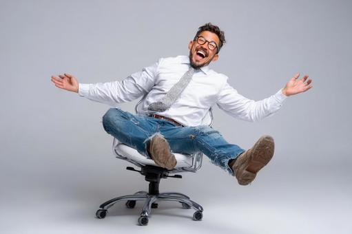 オフィスチェアで楽しげに笑うビジネスマン オフィスチェアで楽しげに笑うビジネスマンの写真