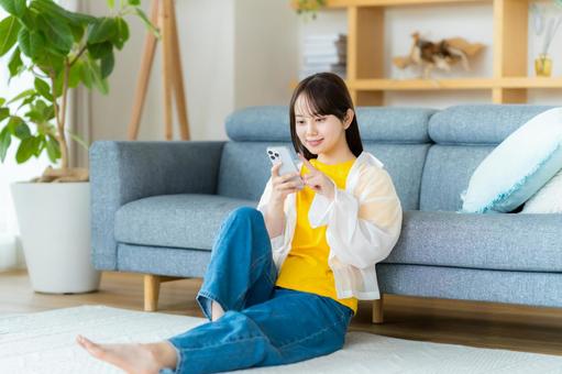 部屋でスマホを操作する若い女性 部屋でスマホを操作する若い女性 スマホ,若い女性,笑顔の写真素材