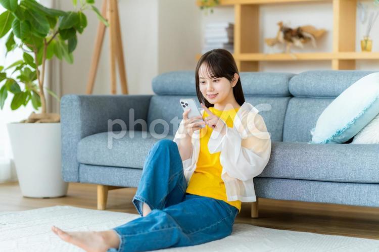 部屋でスマホを操作する若い女性 スマホ,若い女性,笑顔の写真素材