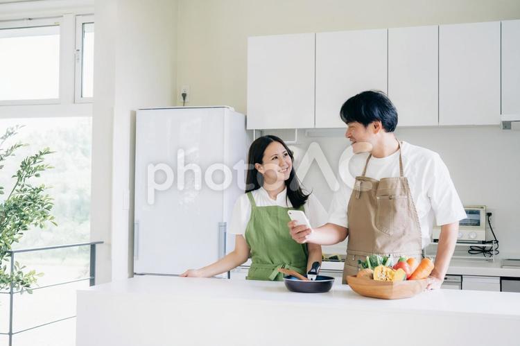 スマホを見ながら料理する男女（笑顔） 料理,家事,レシピの写真素材