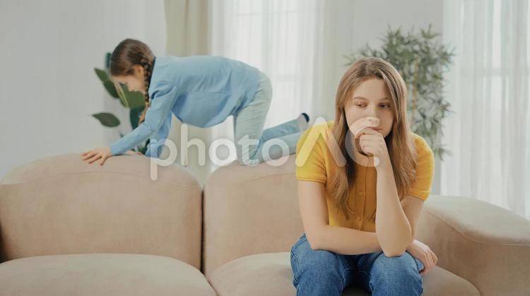座って座って考える女性と後ろを登って遊ぶ女の子 親子,女の子,娘の写真素材
