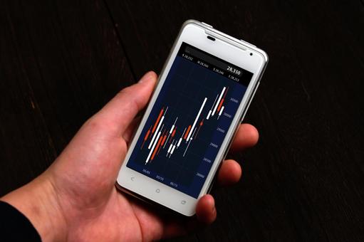 スマホで株価チャートを見る手 スマホで株価チャートを見る手 スマートフォン,株価チャート,手の写真素材