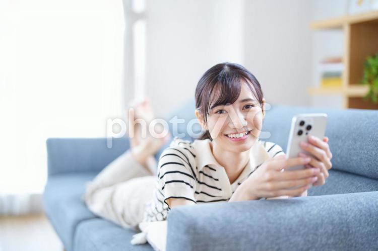 寝転びスマホを持つカメラ目線の女性 女性,スマートフォン,持つの写真素材