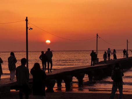 沈む夕陽を桟橋から眺める人達 原岡海岸,岡本桟橋,夕景の写真素材