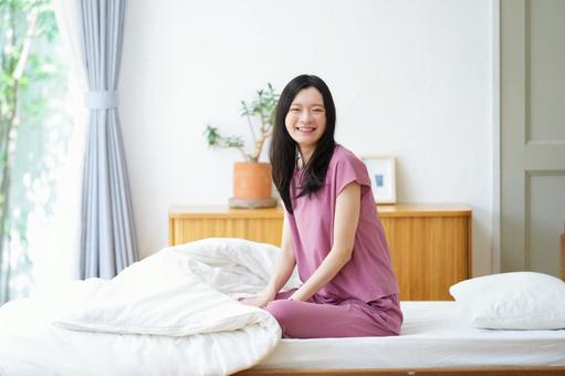 ベッドに座り振り向き笑顔でカメラ目線の女性 女性,笑顔,笑うの写真素材