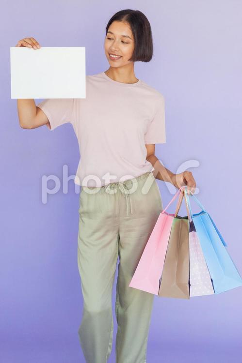 セールで買った物が入った紙袋を持って白い紙を見せる笑顔の女性 セール,ショップ,女性の写真素材